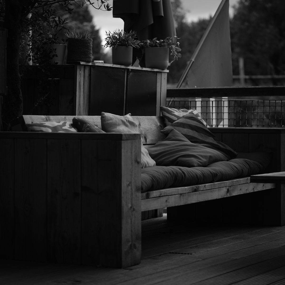 Wooden outdoor sofa with pillows and blanket.