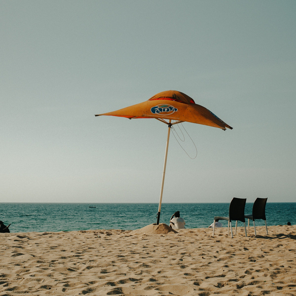 Orange umbrella and chairs on a sandy beach.